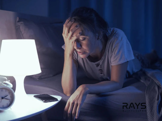 Tired woman sitting on bed at night with hand on forehead, struggling to sleep